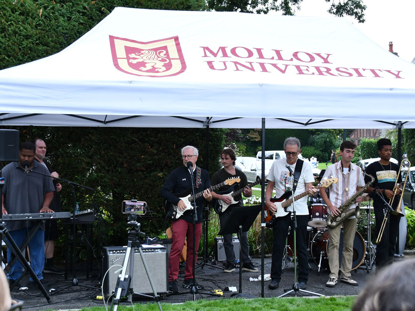 President Jim Lentini holding a guitar performing with band at Molloy University Community Day